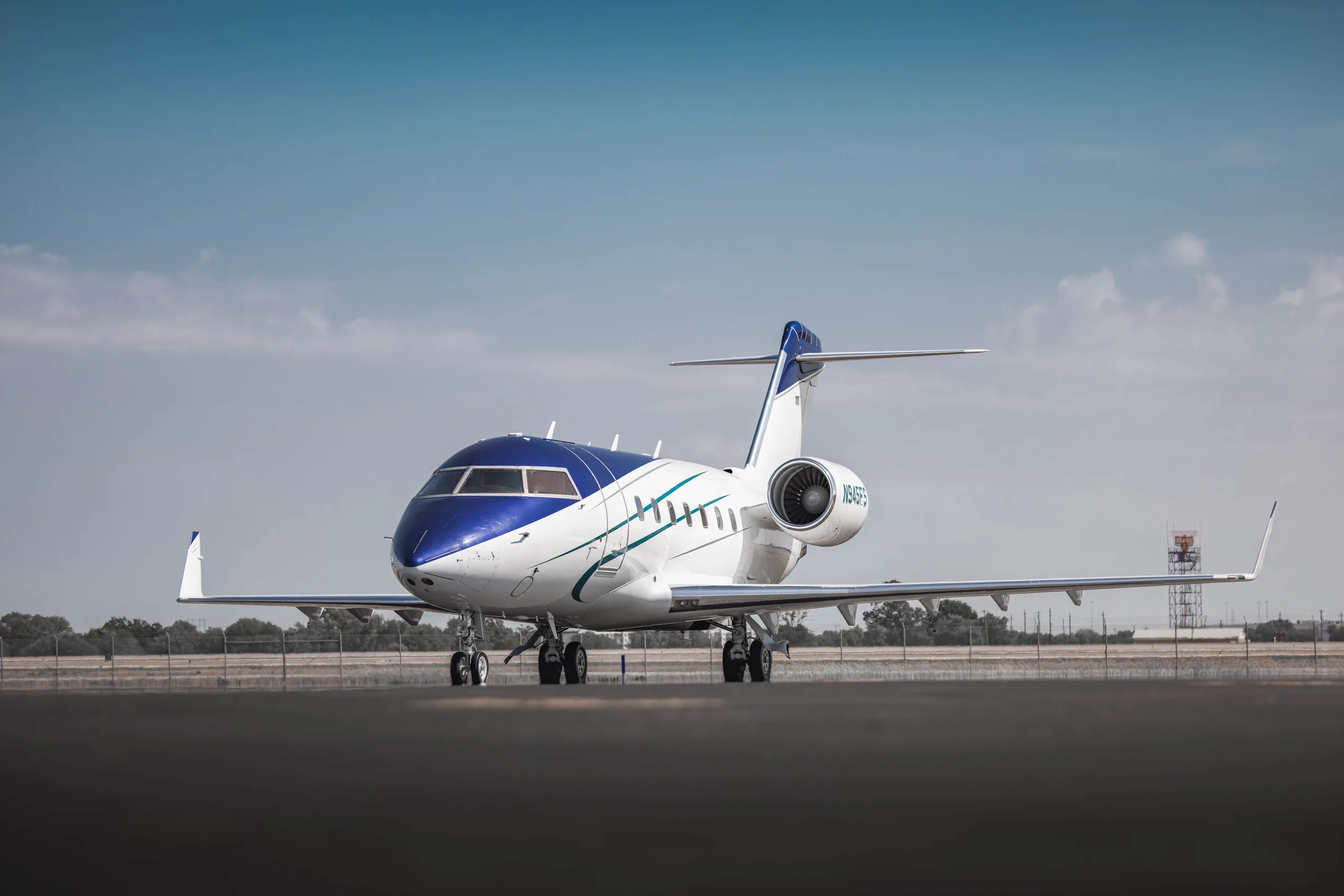A white and blue private jet with green stripes is parked on an airfield under a clear sky.