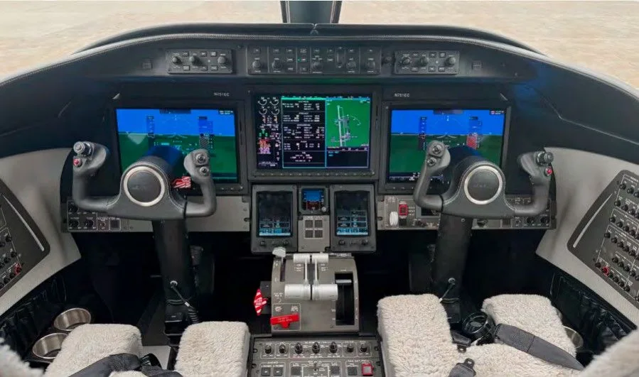 The cockpit of a business jet, featuring multiple large display screens and dual yokes.