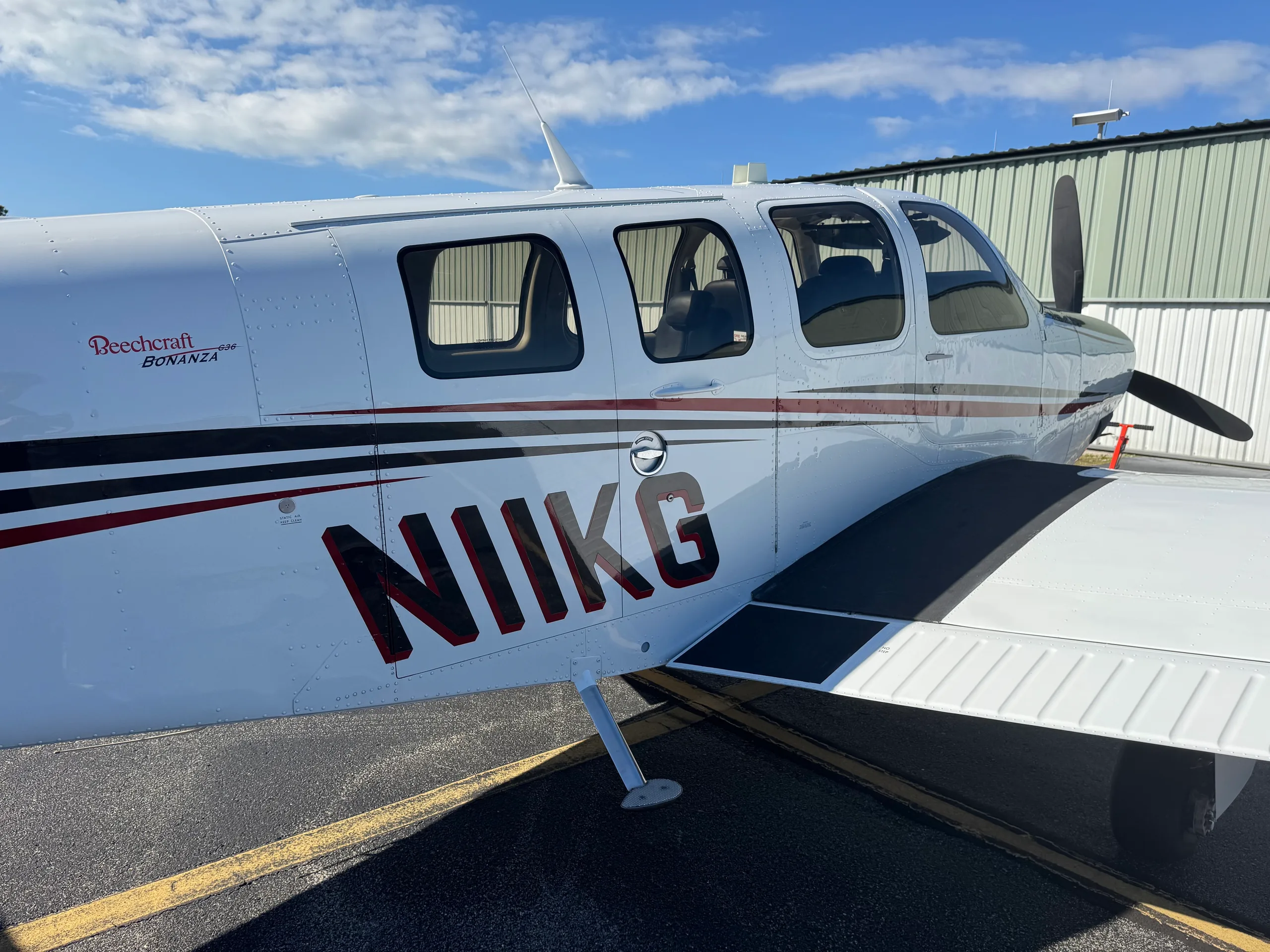 A close-up of the fuselage of Beechcraft Bonanza N11KG, showing its white, black, and red paint scheme.