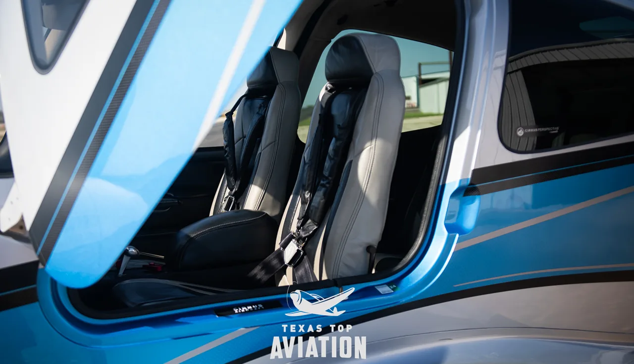 The interior of the Cirrus SR22 aircraft cabin, showing two front seats with black and light grey upholstery through an open door.