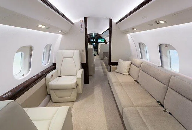 An aircraft cabin interior featuring a long beige sofa on one side and individual light-colored seats on the other.