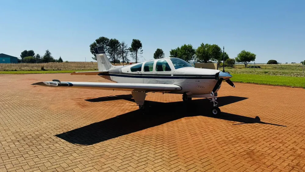 A white and dark grey single-engine propeller aircraft parked on a brick-paved apron under a clear sky.