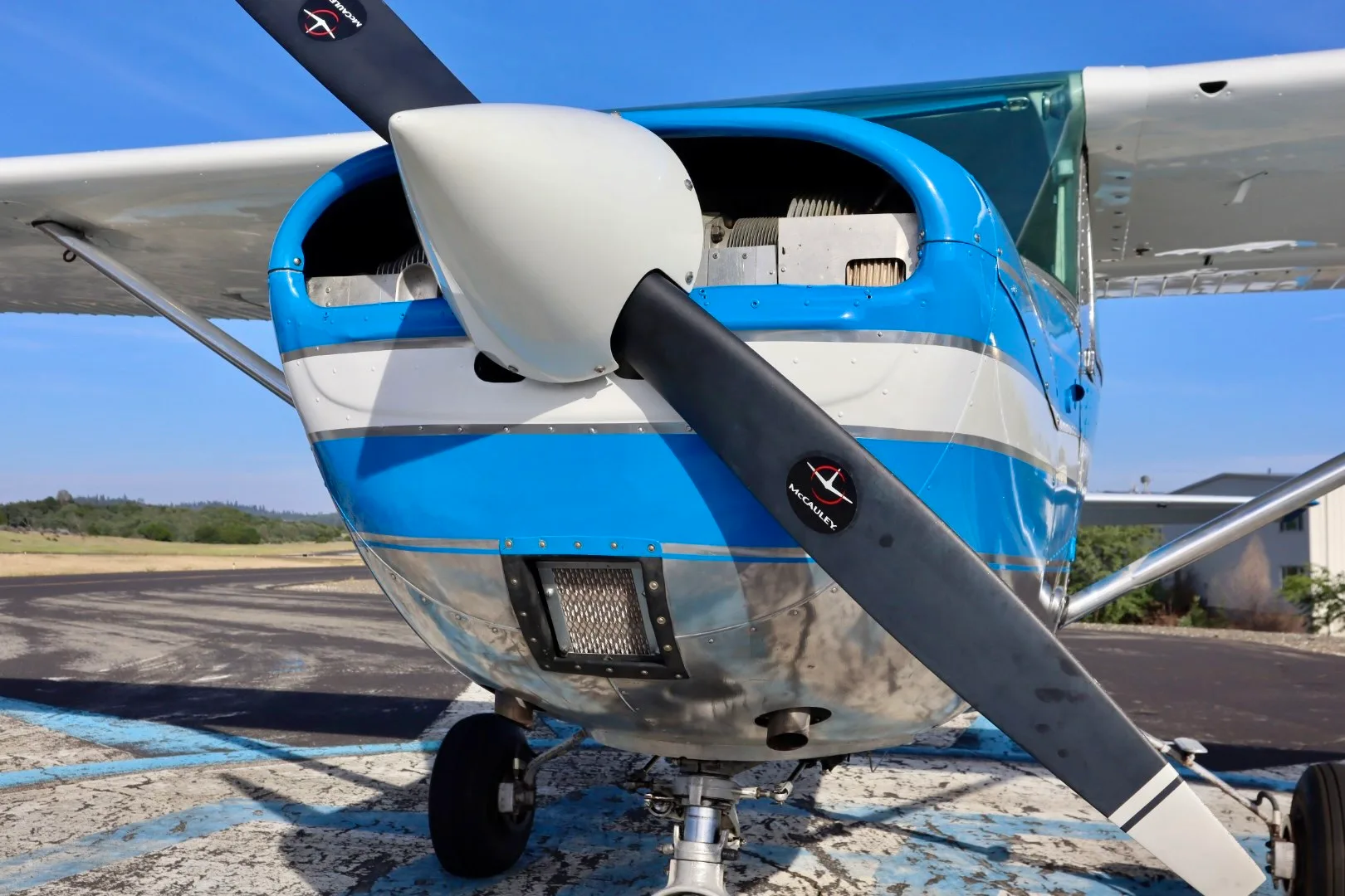 A close-up view of the propeller and nose of a blue and silver Cessna 150 aircraft.