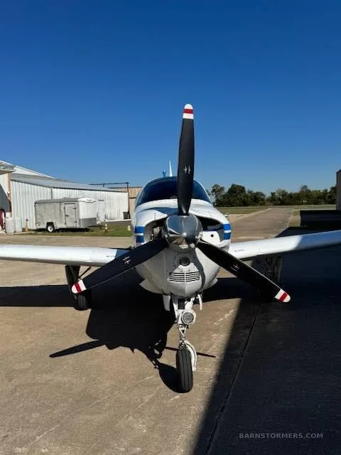 A front view of a white and blue Beechcraft Baron N1124A showing its propeller and nose gear.