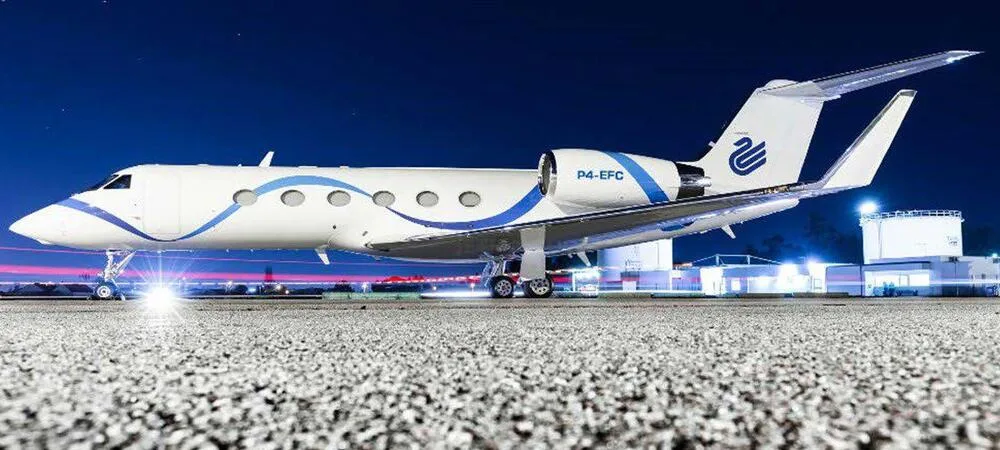 A Gulfstream G450 business jet with a white and blue wavy paint scheme on an airfield at night.