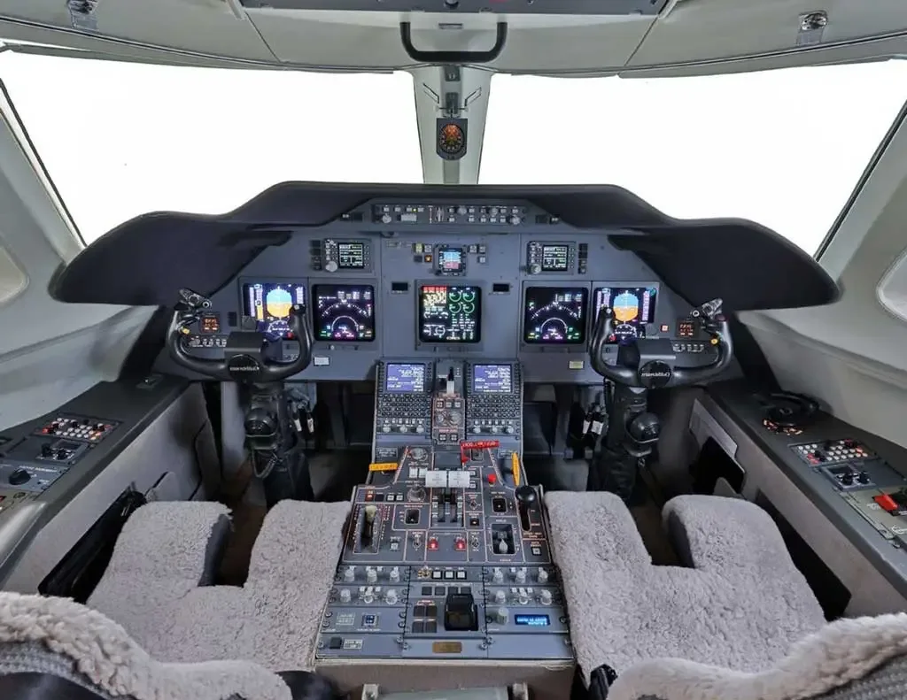 The cockpit of a modern business jet, featuring multiple digital displays, control yokes, and a central throttle quadrant.