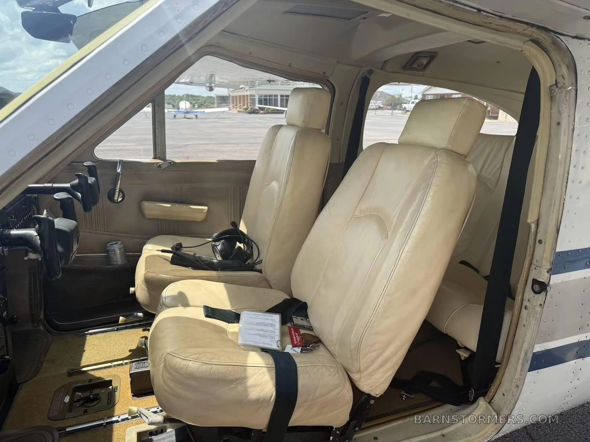 The light tan leather front seats of a small aircraft cabin, with a headset on the left seat.