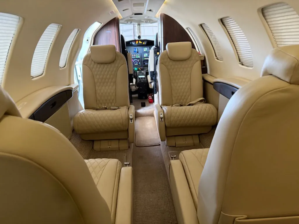 View from the rear of a private jet cabin, showing quilted beige leather seats and the cockpit in the distance.