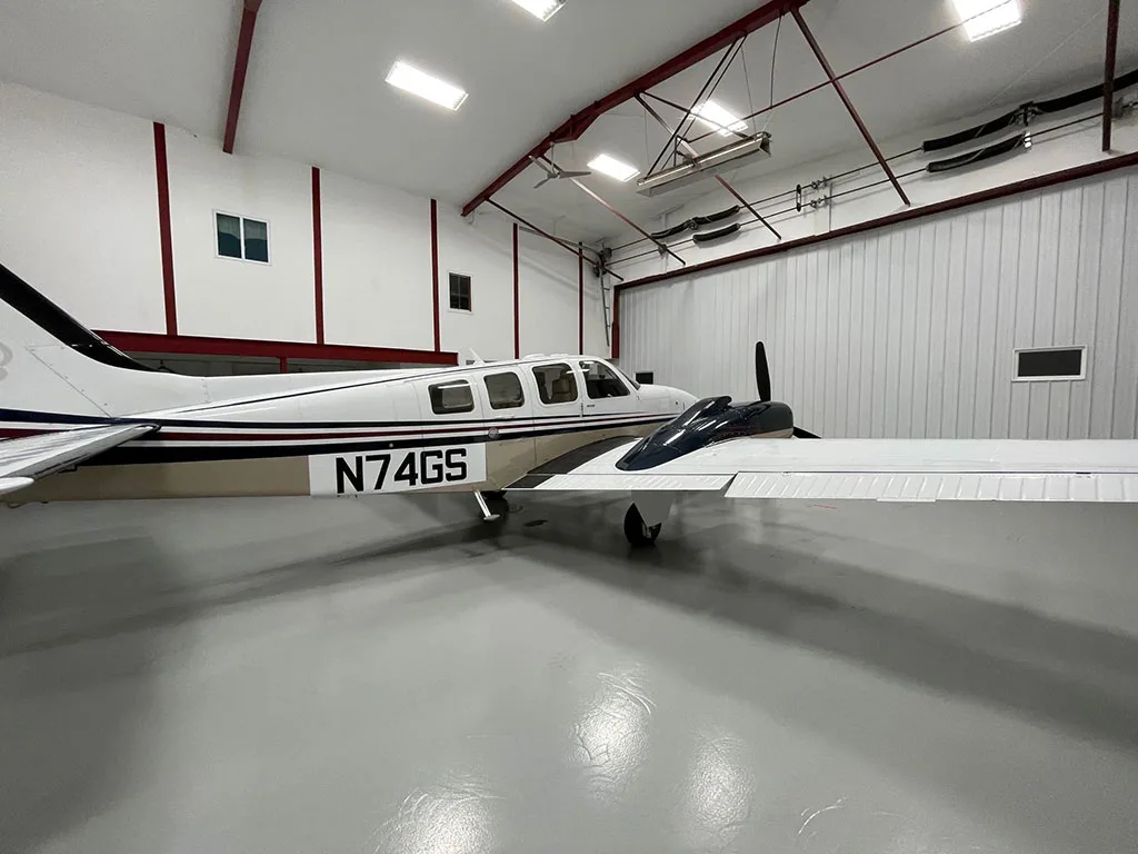 A side view of the white and tan twin-engine aircraft N74GS with dark blue and red stripes, parked in a hangar.