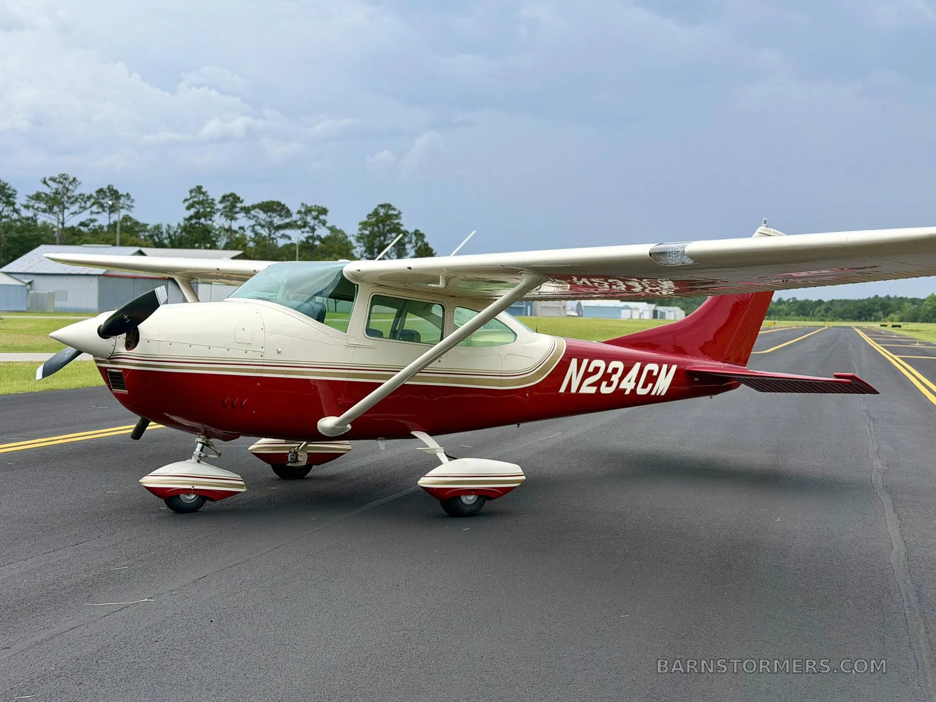 A side view of a red and white single-engine high-wing aircraft with registration N234CM parked on an airfield tarmac.
