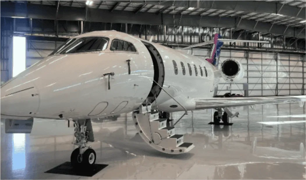 A white business jet with its main entry door open and stairs extended, parked inside a large hangar.