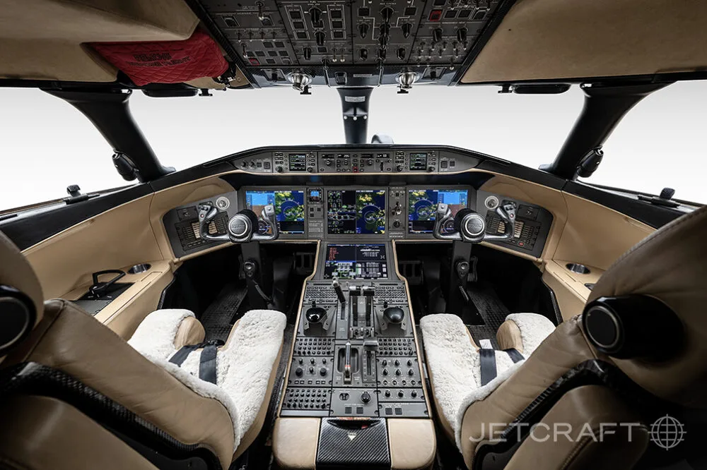 The modern cockpit of a Bombardier Global business jet, featuring multiple digital displays and tan leather seats.