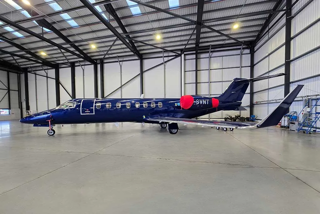 A dark blue private jet with registration G-SVNT and red engine covers parked in a hangar, viewed from the side.