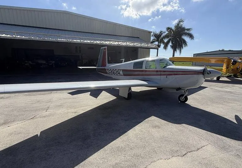A white single-engine aircraft with red stripes, registration N9292M, parked on an airfield with palm trees.