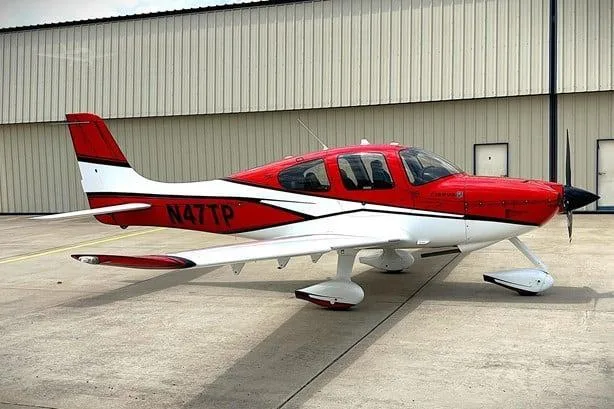 A red and white Cirrus SR22 aircraft, registration N47TP, parked on an asphalt apron in front of a hangar.