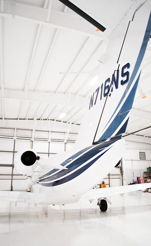 A close-up view of the tail of a white business jet (N716NS) with blue stripes in a hangar.