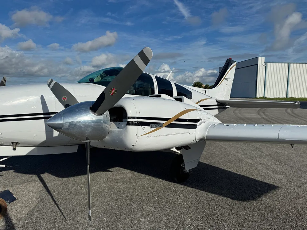 A close-up view of the right engine and front fuselage of a white Beechcraft Baron aircraft with black and gold stripes.