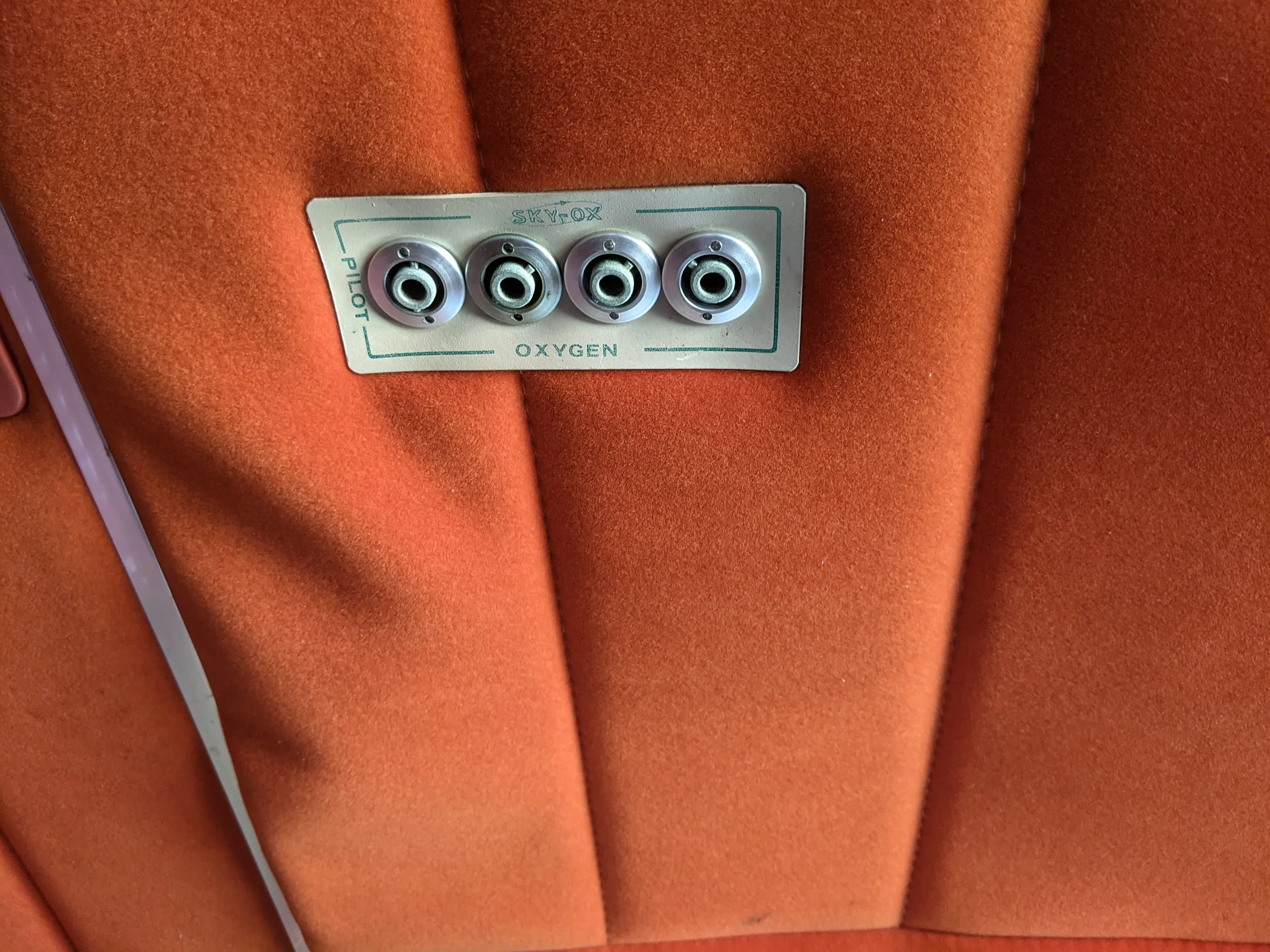 A close-up of an oxygen port panel labeled "SKY-OX" on the orange fabric ceiling of the aircraft interior.