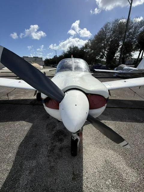 A head-on view of the white Piper Cherokee aircraft, highlighting its propeller and engine cowling.