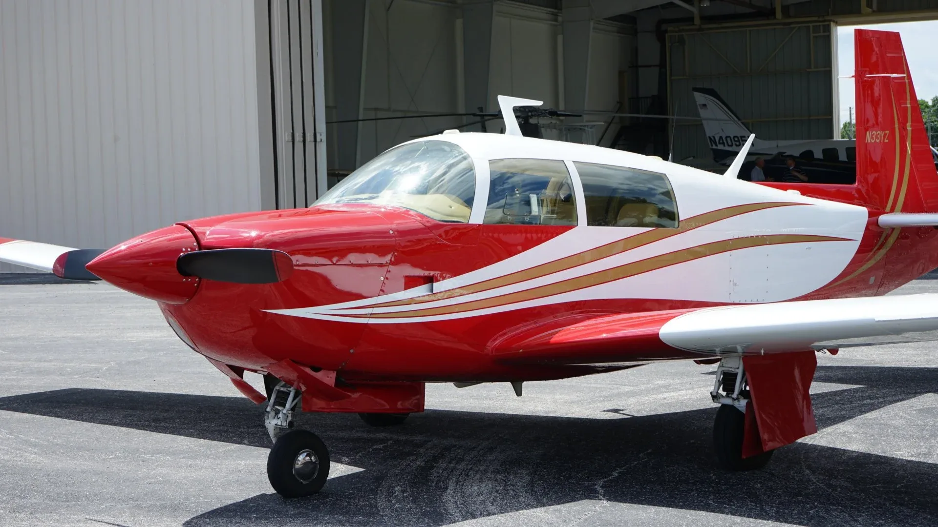 A close-up view of the front-right side of a red and white single-engine aircraft with gold stripes.