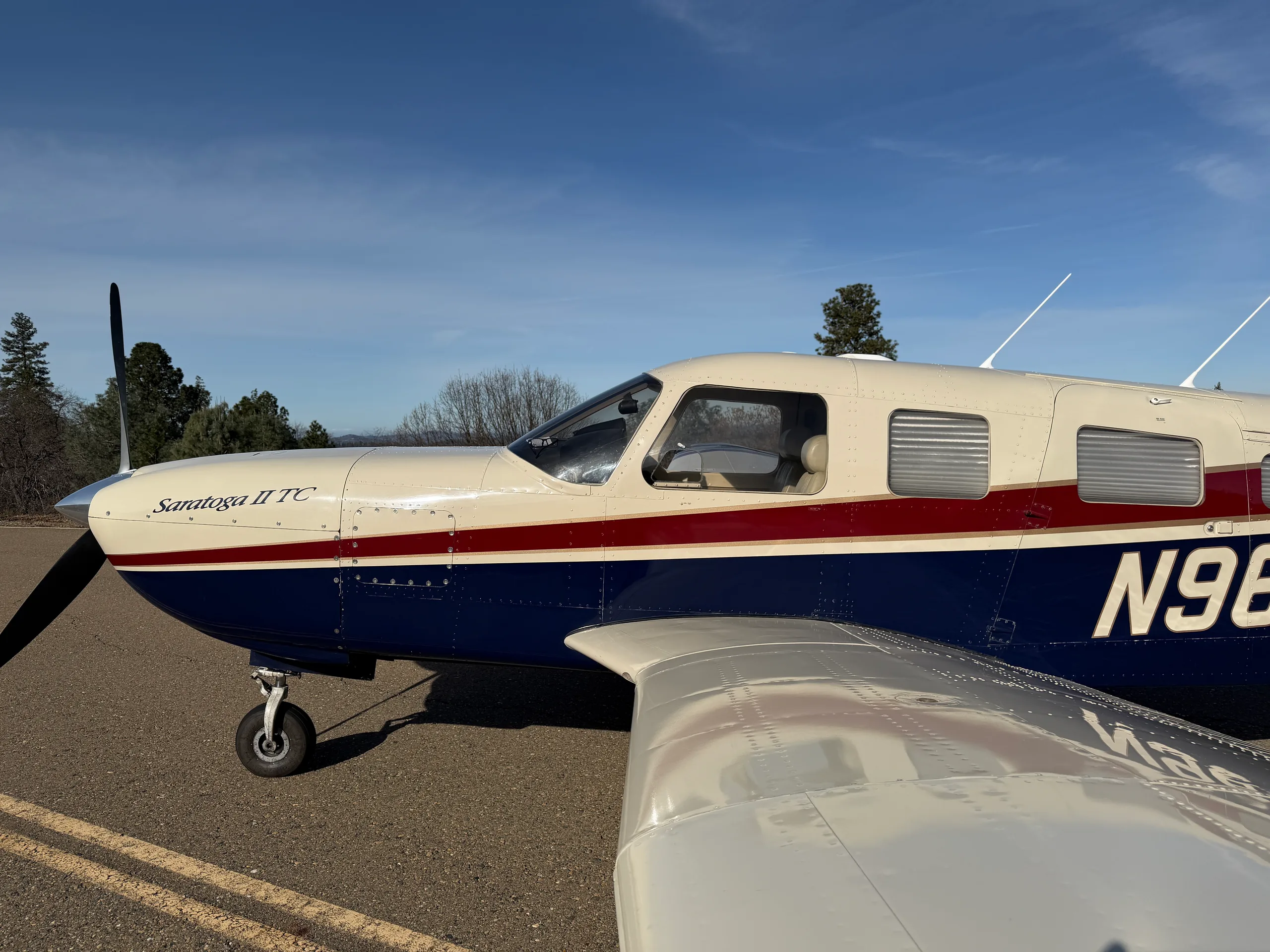 A close-up side view of the Piper Saratoga II TC aircraft showing the cream, blue, and red fuselage and registration N965BJ.