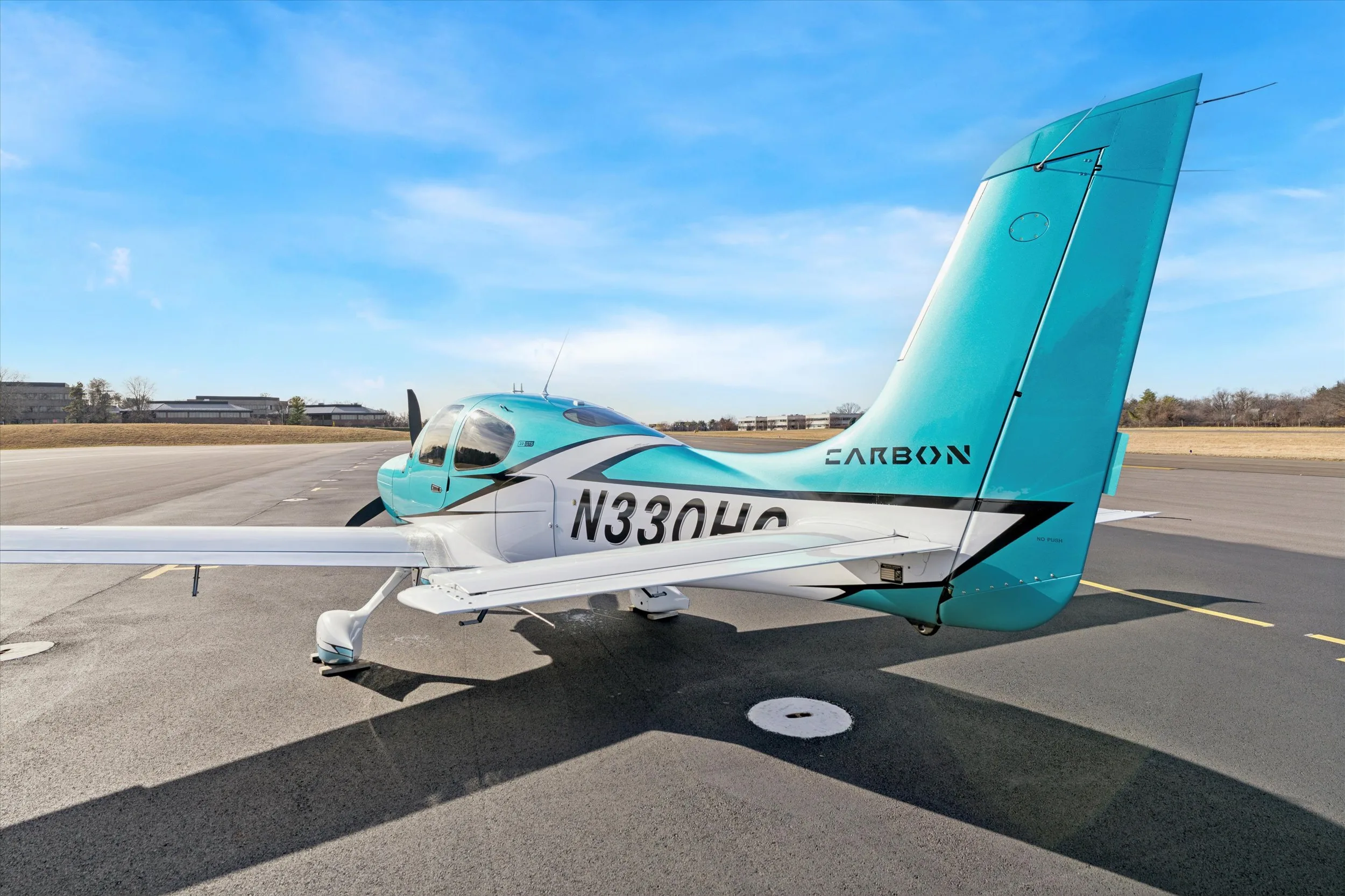 A rear-quarter view of a teal and white Cirrus SR22 aircraft, registration N330HC, showing the tail and right wing on an airfield.