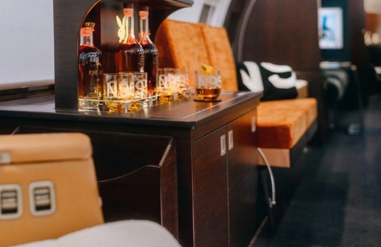 A close-up of a well-stocked bar cabinet in the private jet's cabin, featuring bottles of liquor and glasses.