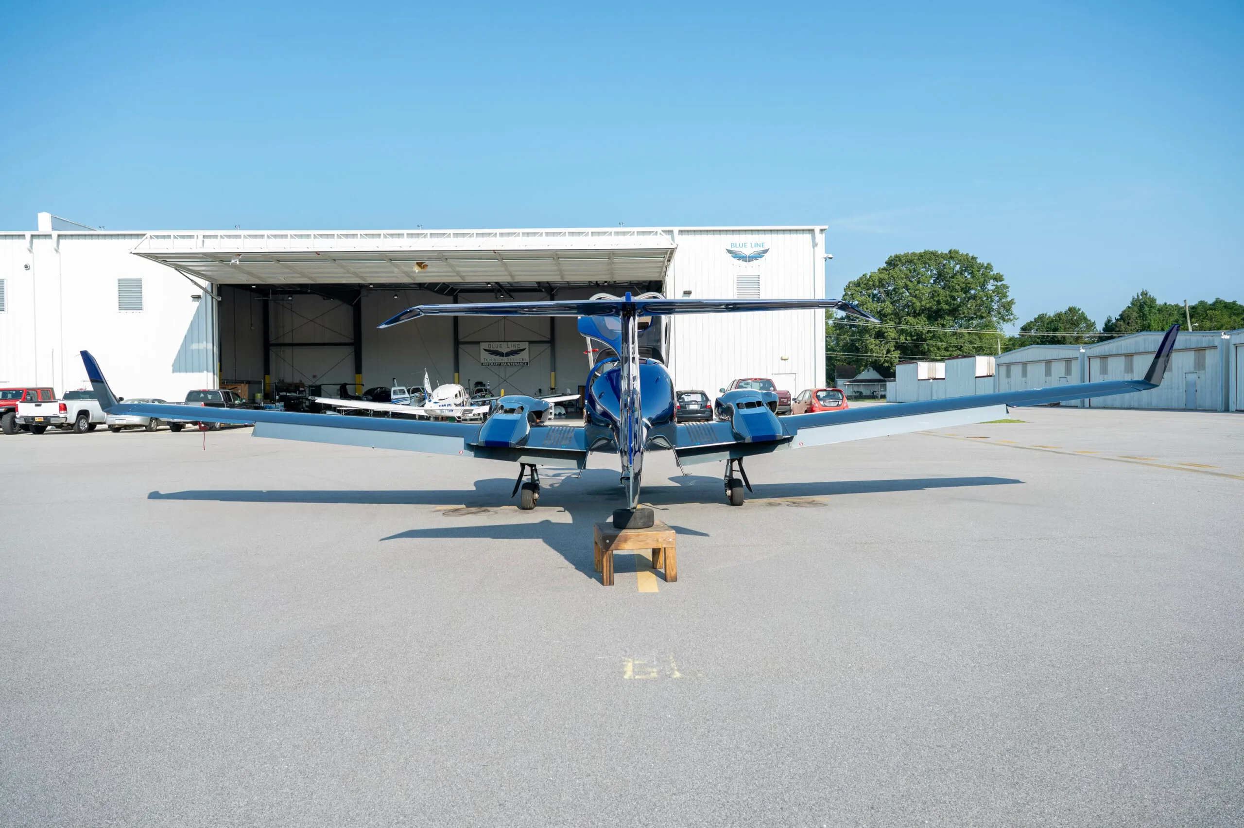 Rear view of a blue and grey Diamond DA42 aircraft parked in front of a hangar.
