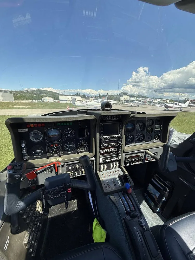 The cockpit of the Socata Trinidad aircraft, showing the instrument panel and controls with an airfield in the background.