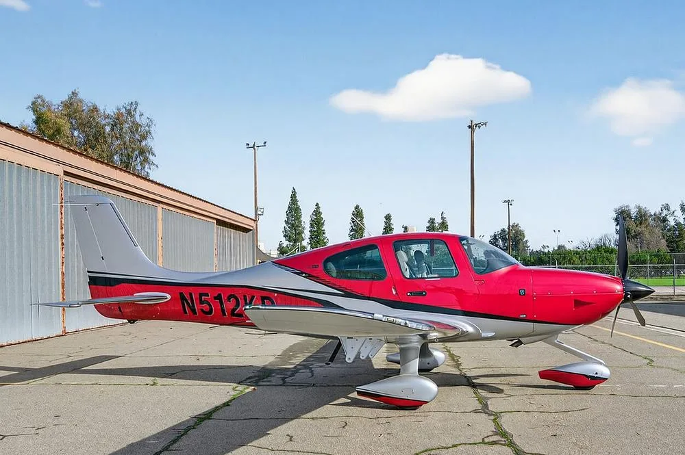 A side view of a red and silver single-engine aircraft, N512KP, with its doors closed, parked on an airfield.