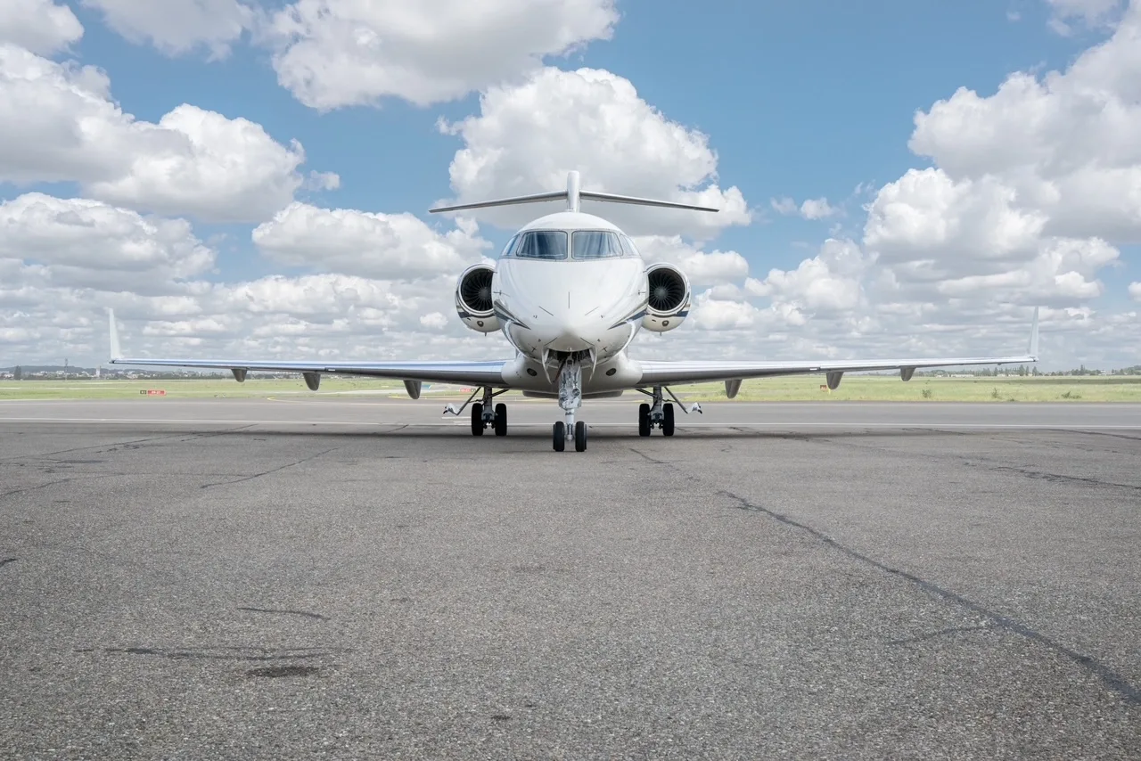 A white Bombardier Challenger 300 business jet seen head-on on an airfield under a blue sky.