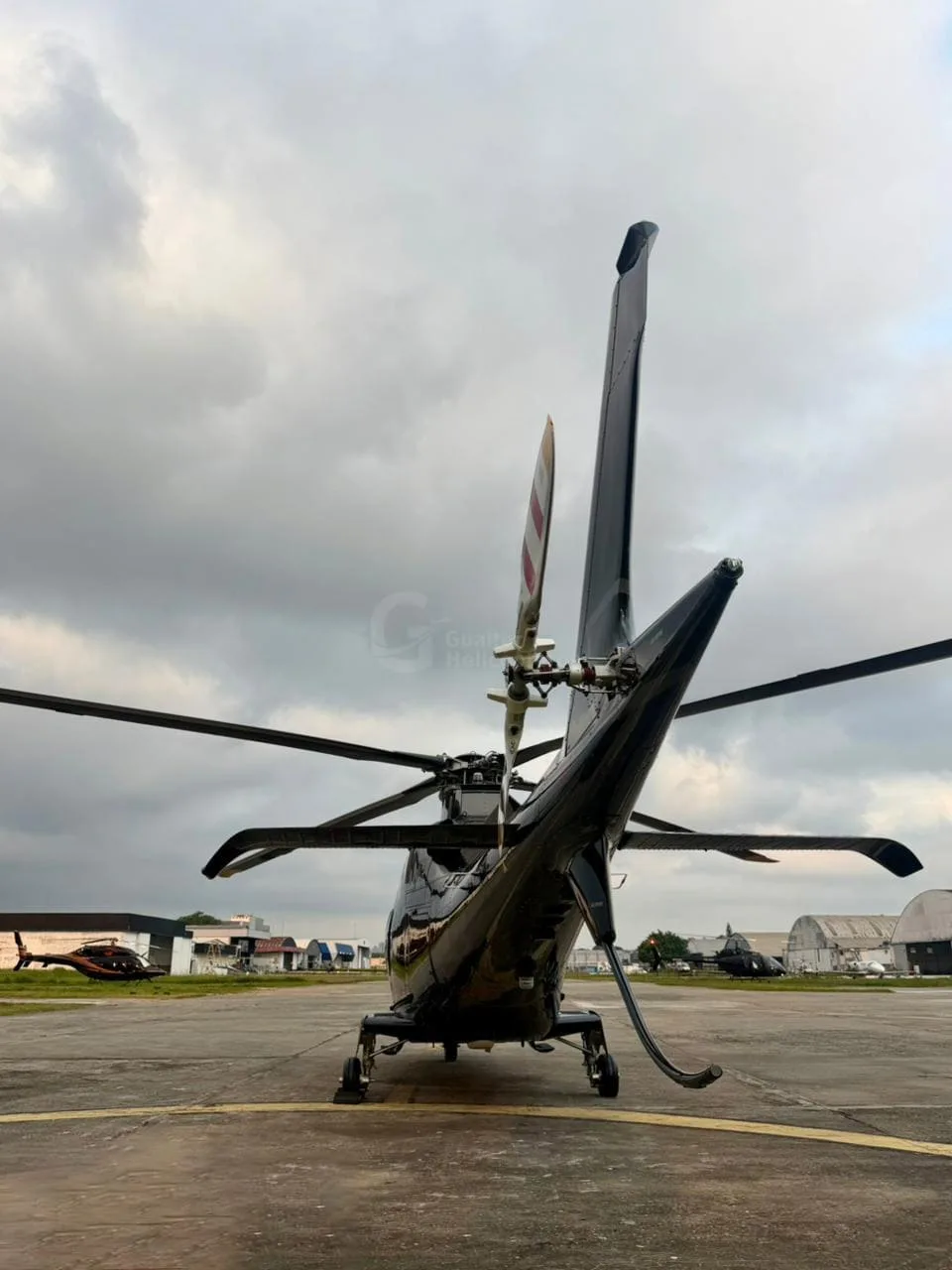 A rear view of a black AgustaWestland AW109 helicopter with its tail rotor visible, parked on an apron.