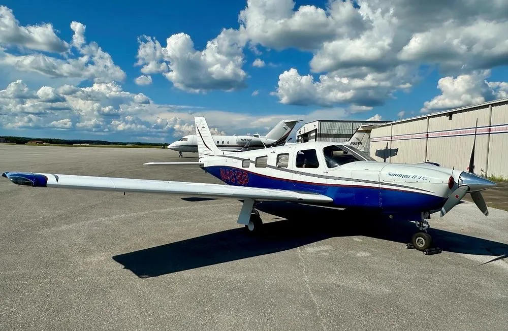 A Piper Saratoga II TC aircraft, registration N401BP, in white and blue paint, parked on an asphalt ramp under a partly cloudy sky.