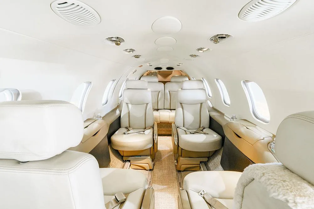 A view looking forward into the aircraft cabin, showing rows of light-colored leather seats and windows.