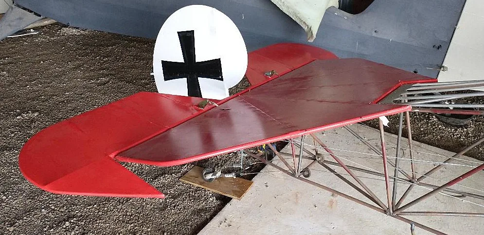 A close-up of the red tail section of a triplane with a white roundel and black German cross insignia.
