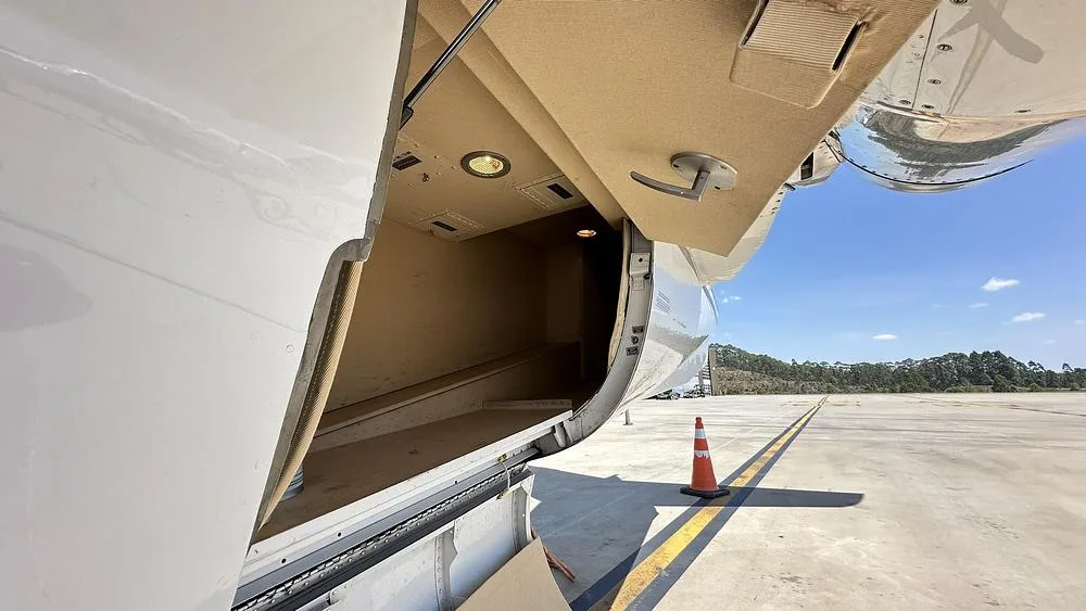 An open baggage compartment on the side of a white business jet, revealing a beige interior.