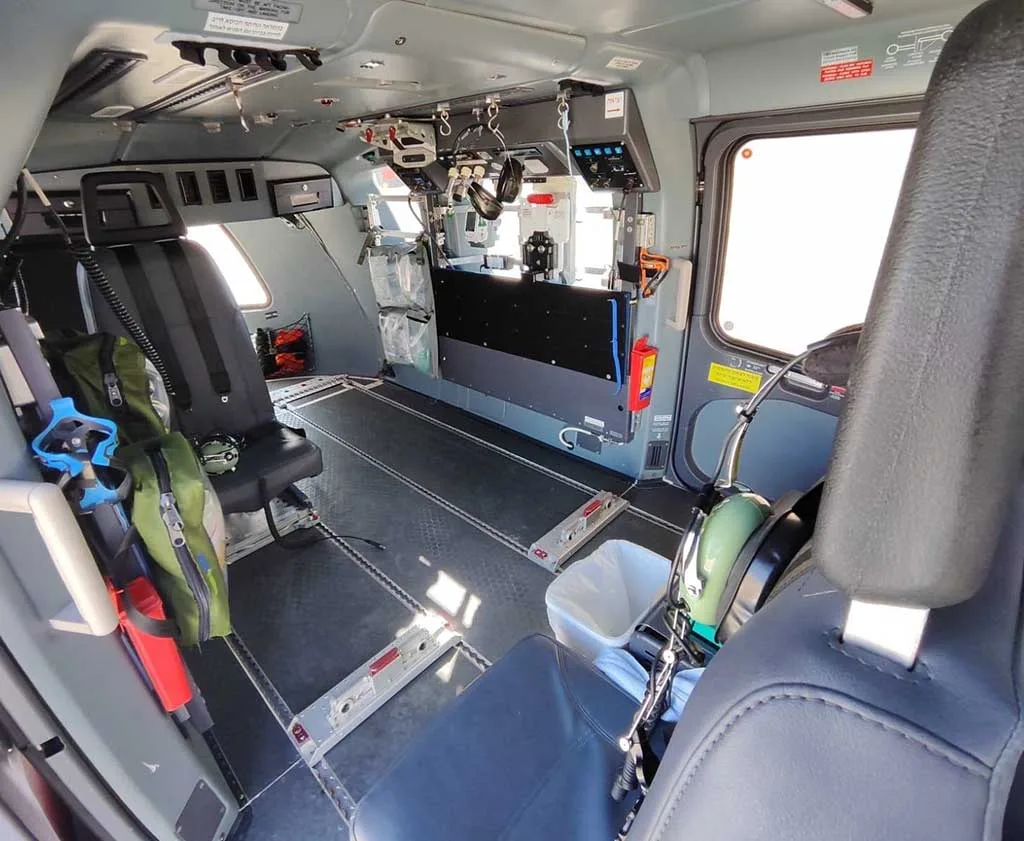 The interior cabin of a helicopter, showing a utility configuration with a single seat and various equipment mounted on the walls.