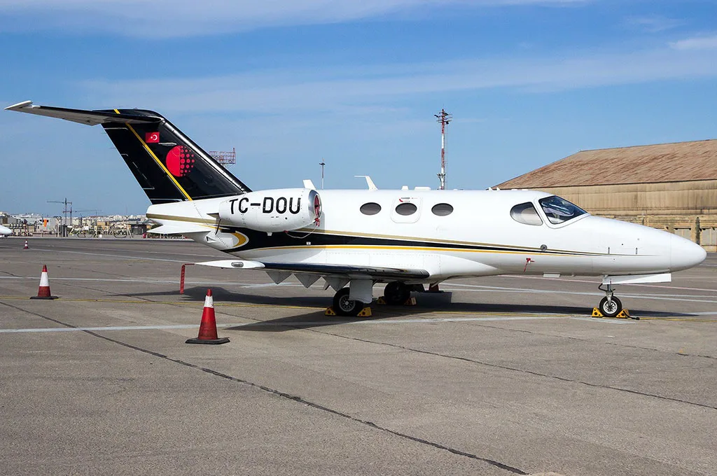 A white business jet with black and gold accents on the tail and fuselage, registration TC-DOU, parked on an airport tarmac.