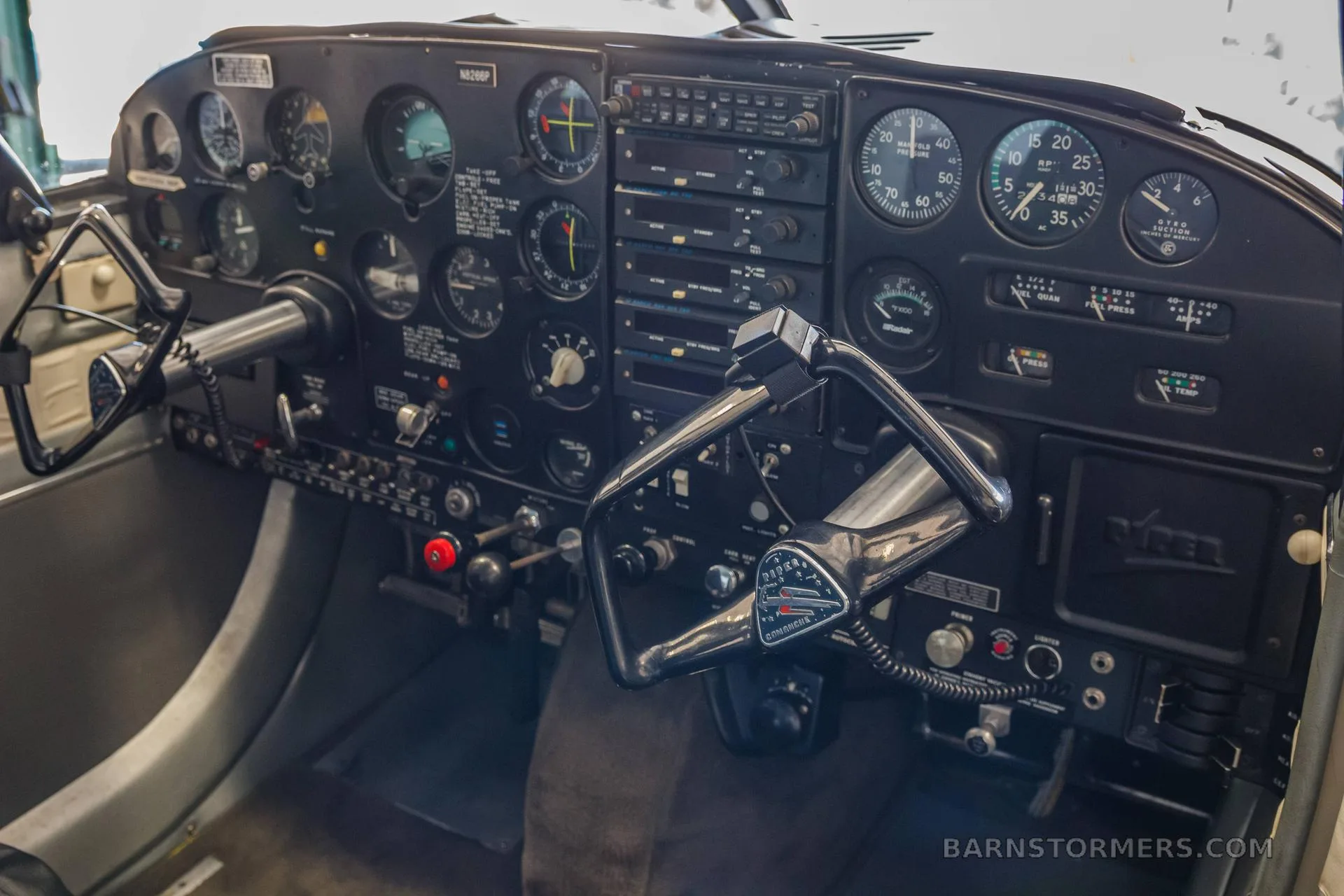 The cockpit of a Piper Comanche 250 shows the instrument panel, yokes, and radios.