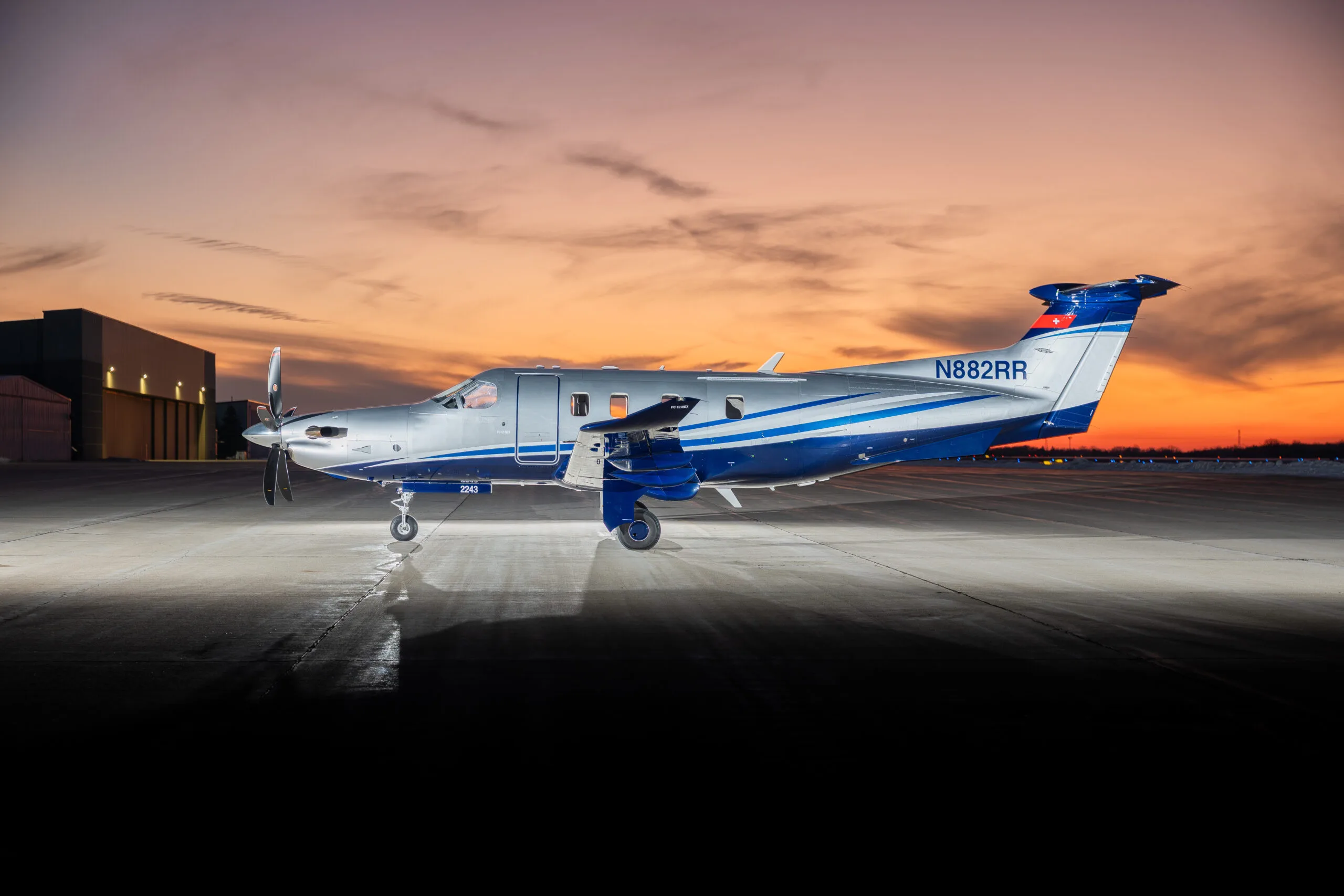 A silver and blue Pilatus PC-12 turboprop aircraft with registration N882RR parked on a tarmac at dusk.