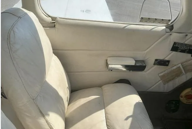 The white leather pilot's seat and interior side panel of a small aircraft.