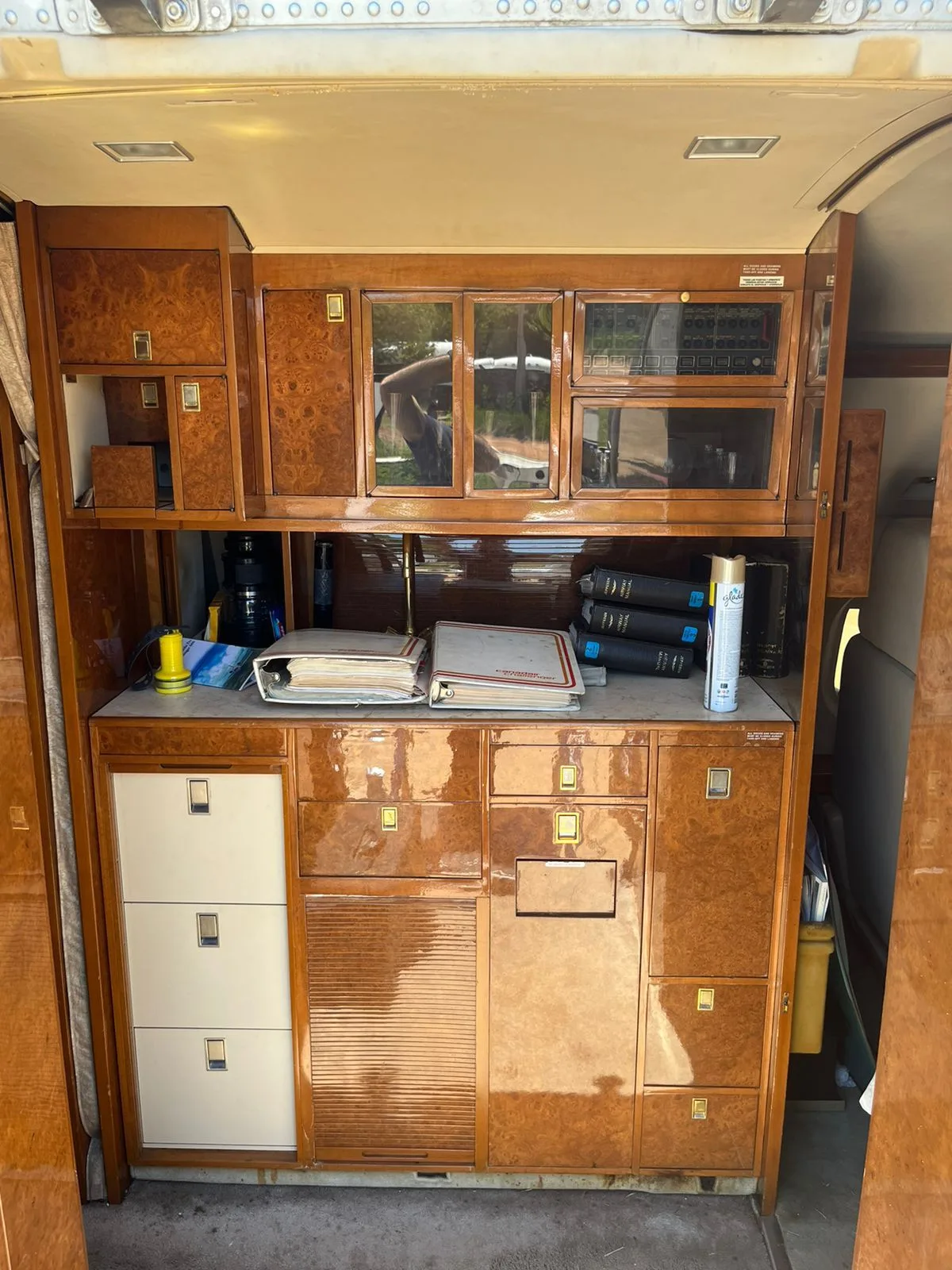 A detailed view of a wooden cabinet and galley area inside a business jet, with various items stored.
