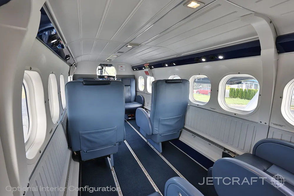 An aircraft interior showing blue seats, windows, and the cabin ceiling from a side angle.
