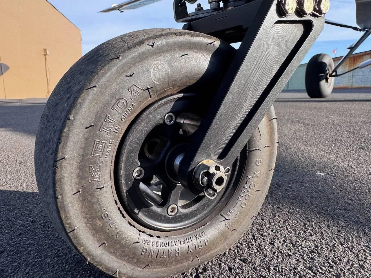 A close-up of a large tundra tire and black landing gear strut on an aircraft, showing tire details.