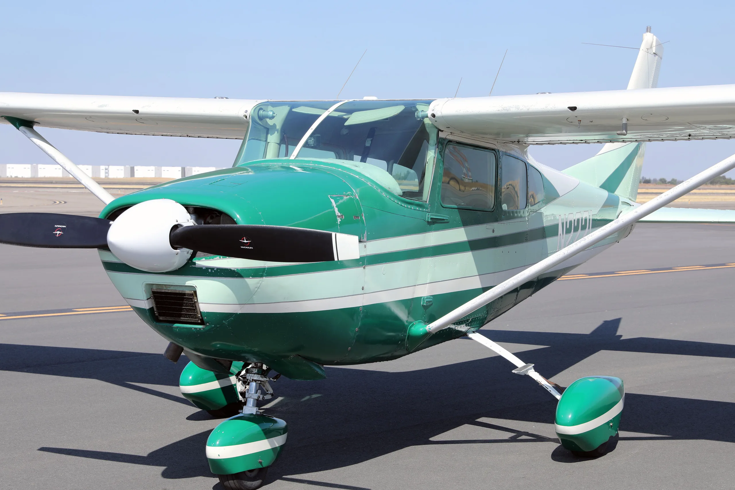 A close-up front-quarter view of a green and white Cessna 182 Skylane N2221 on an airfield.