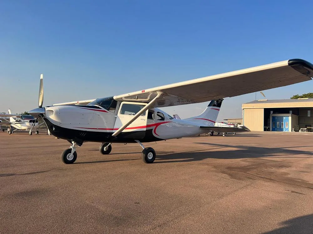 A white and black Cessna aircraft with red stripes is parked on an airfield under a clear sky.