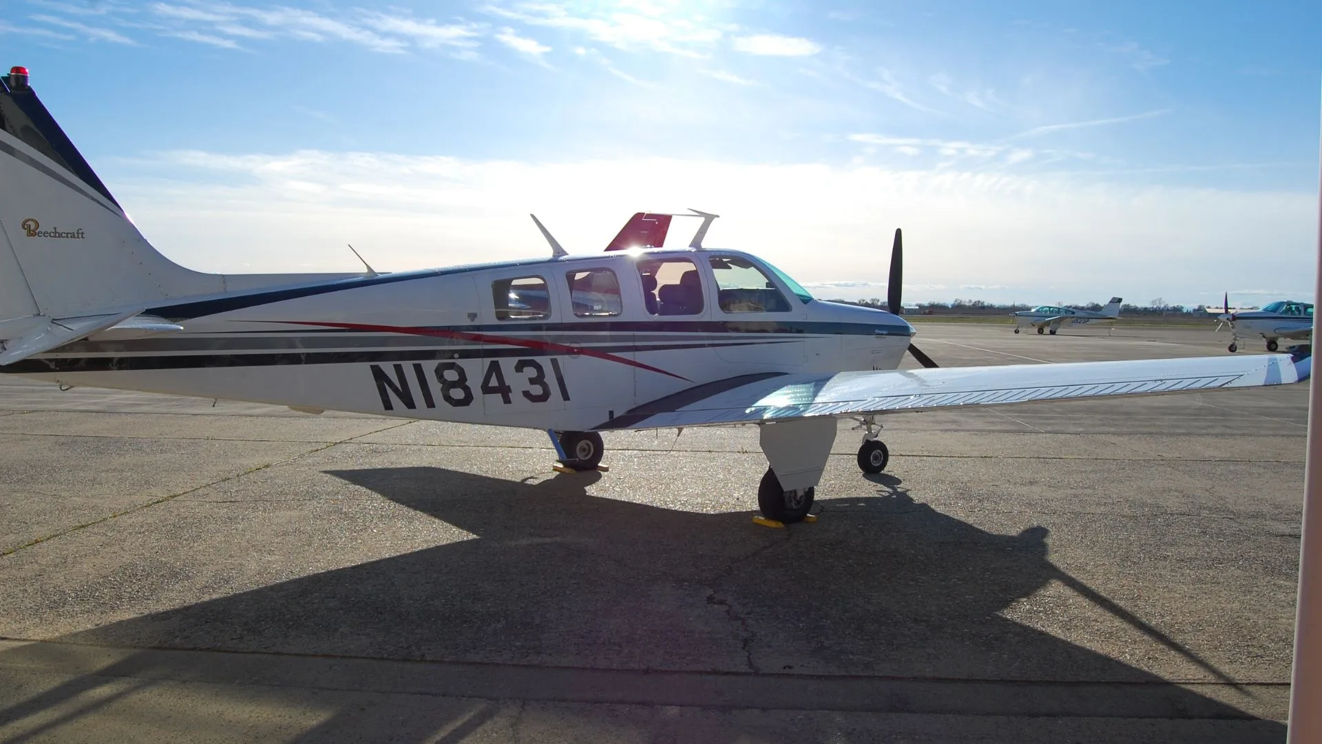 Side view of a Beechcraft Bonanza with white and gray paint scheme, parked on the tarmac.