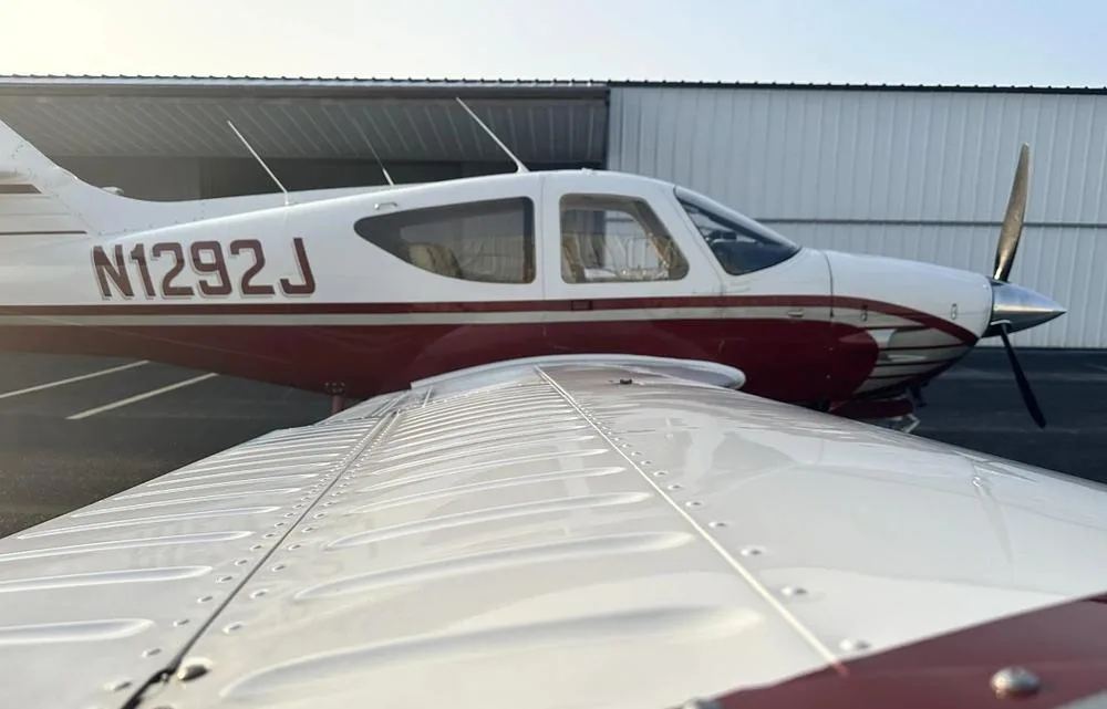 A close-up view of the wing and fuselage of the white and red aircraft N1292J, parked outdoors.