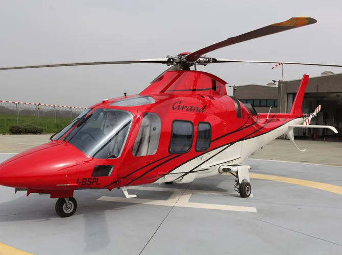 A red and white AgustaWestland AW109 Grand helicopter with registration I-BSPL parked on a helipad.