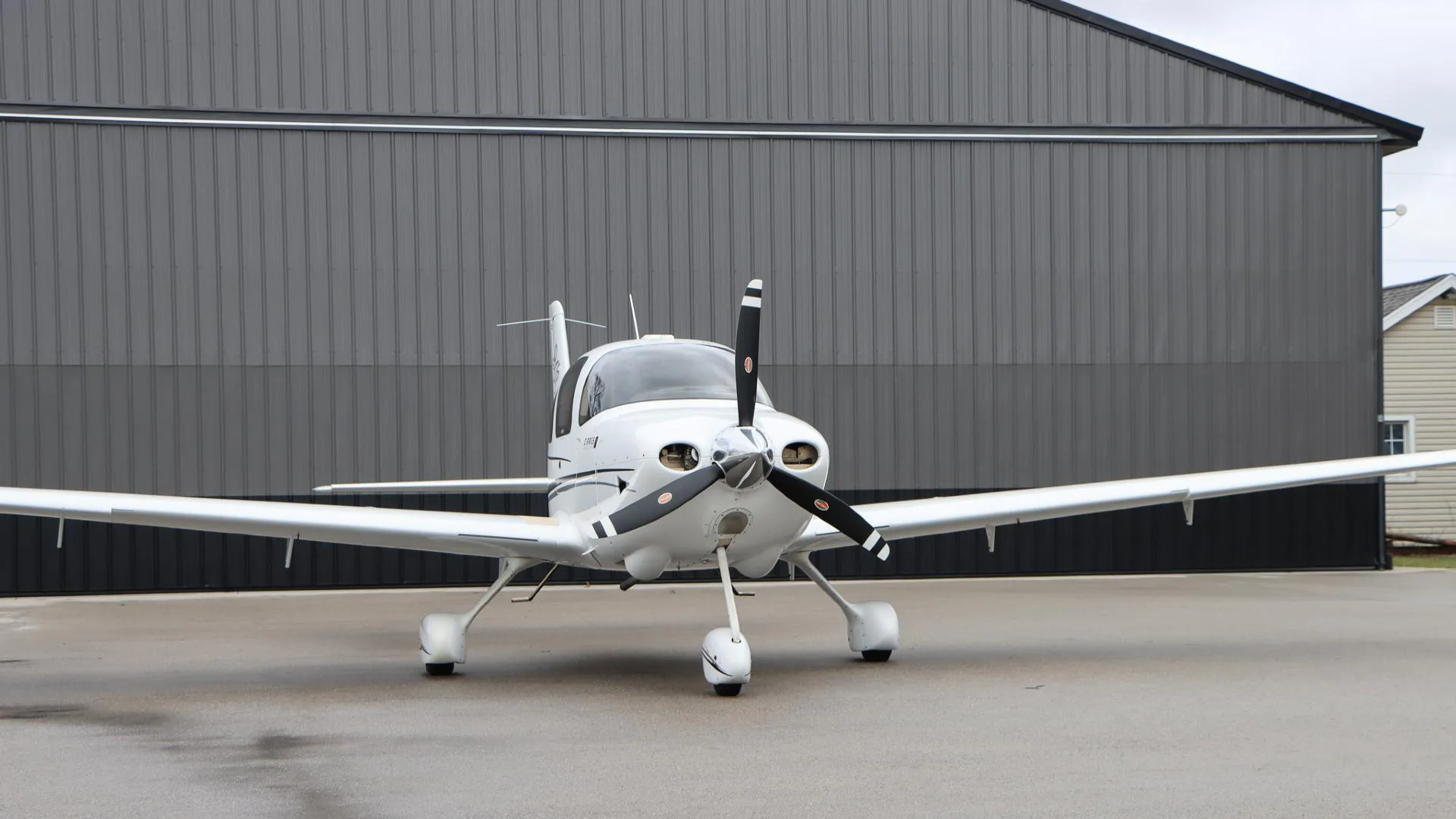 A white Cirrus SR20 GTS aircraft, N984PG, is parked head-on in front of a dark gray hangar.